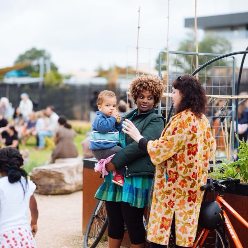 Two parents talking while holding their children beside the garden beds