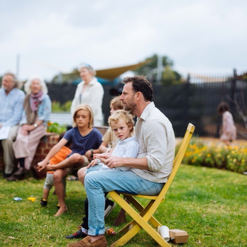 A father sitting on a yellow chair with a small boy on his lap watching the concert