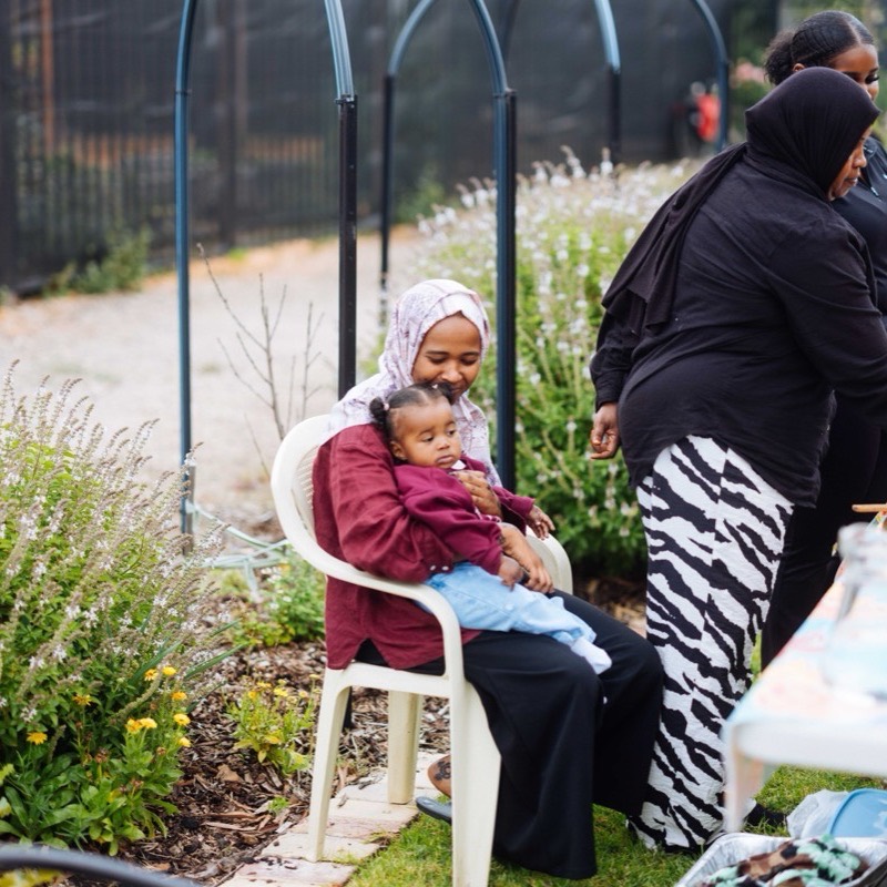 A parent holding a sleepy toddler on a chair beside the herb beds